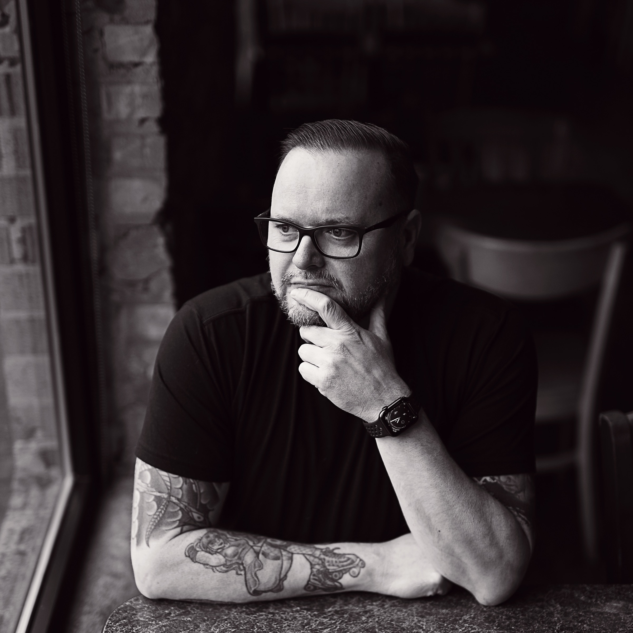 Ryan Knott sitting at a table. He is looking out a window and his head is resting on his hand.